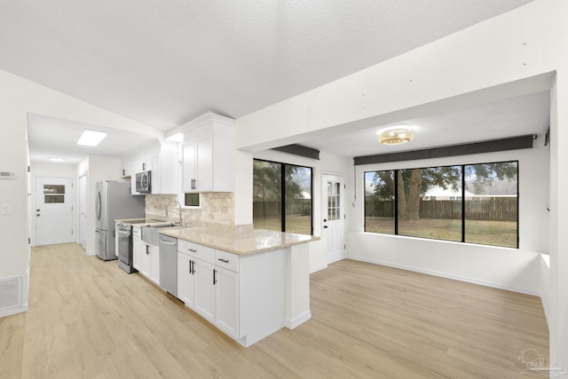 kitchen with light wood-type flooring, white cabinets, stainless steel appliances, light stone countertops, and backsplash