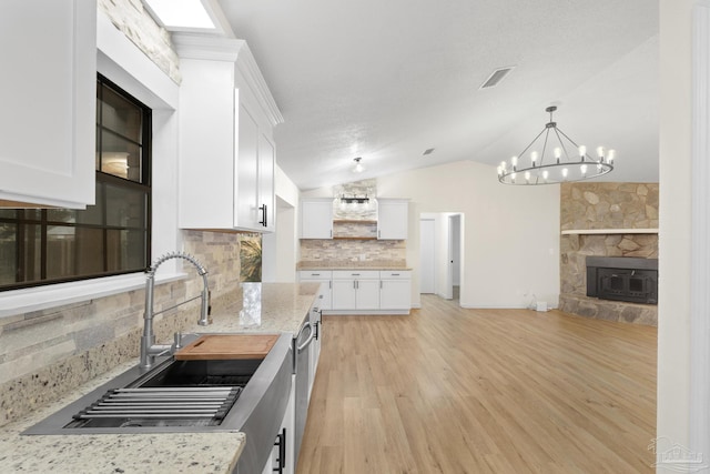 kitchen featuring a stone fireplace, sink, white cabinetry, light stone countertops, and light hardwood / wood-style floors