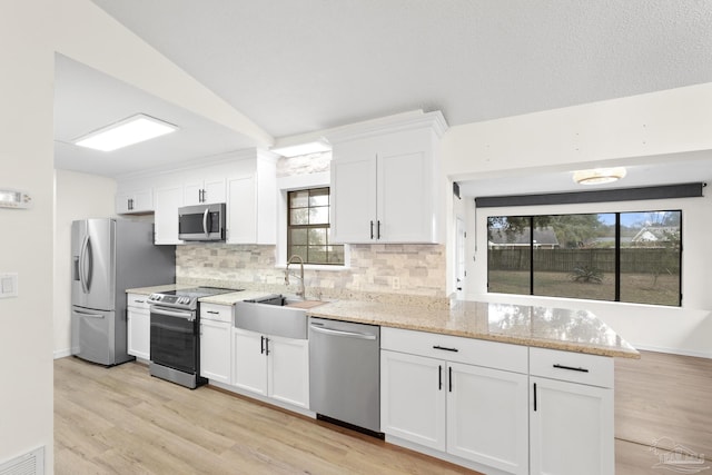 kitchen with appliances with stainless steel finishes, tasteful backsplash, white cabinetry, sink, and light stone countertops