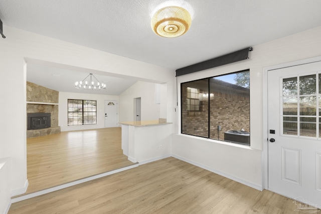 interior space with vaulted ceiling, a fireplace, a notable chandelier, a textured ceiling, and light hardwood / wood-style flooring