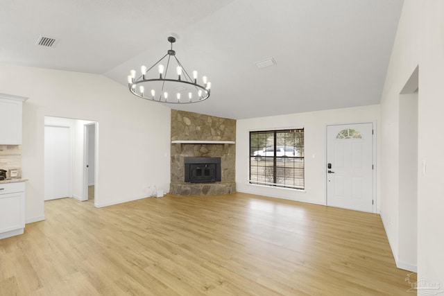 unfurnished living room featuring lofted ceiling, a stone fireplace, an inviting chandelier, and light wood-type flooring