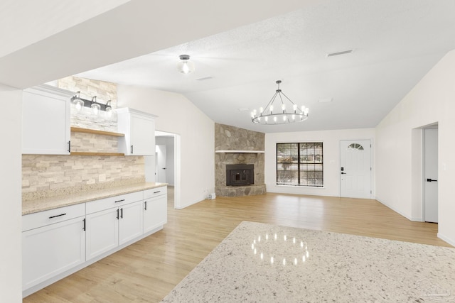 kitchen with light stone countertops, lofted ceiling, white cabinets, and an inviting chandelier