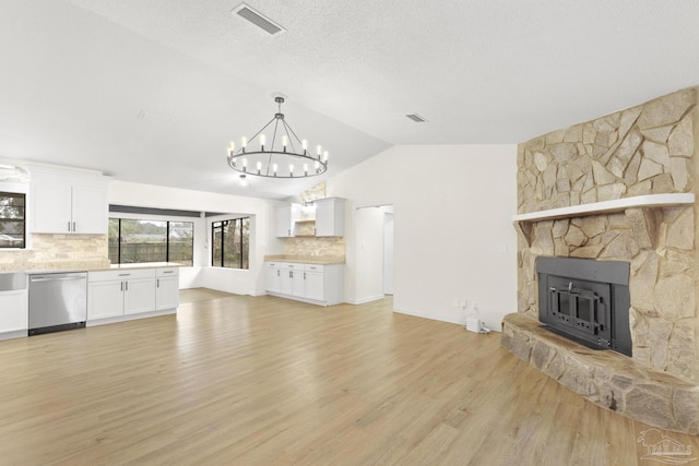 unfurnished living room featuring vaulted ceiling, a stone fireplace, a textured ceiling, and light wood-type flooring