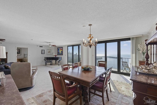 dining area with floor to ceiling windows, ceiling fan with notable chandelier, a water view, light tile patterned floors, and a textured ceiling