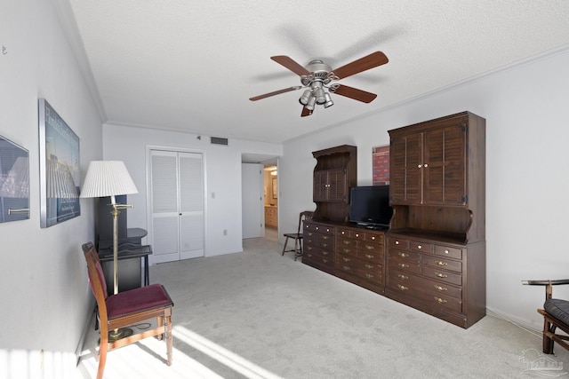 interior space with a textured ceiling, light colored carpet, ceiling fan, crown molding, and a closet