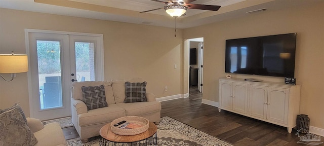 living area featuring a ceiling fan, visible vents, baseboards, dark wood-style floors, and a raised ceiling