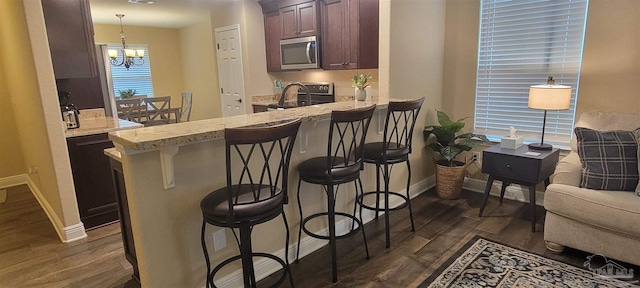 kitchen with dark wood-type flooring, stainless steel microwave, decorative light fixtures, and a breakfast bar area