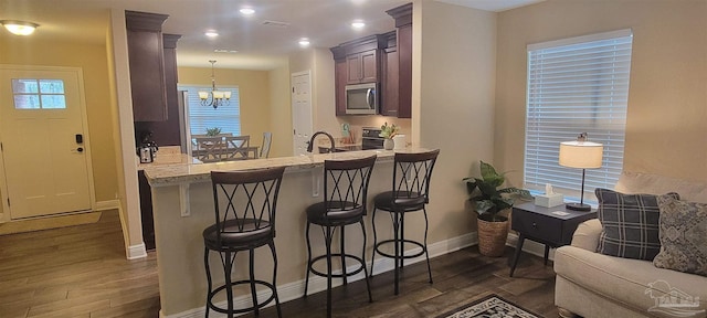 kitchen featuring dark wood-style floors, stainless steel microwave, a peninsula, and a kitchen bar