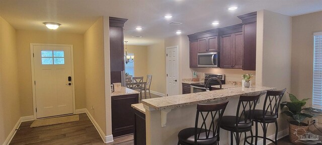 kitchen with a breakfast bar, appliances with stainless steel finishes, light stone countertops, wood-type flooring, and kitchen peninsula