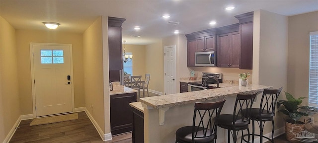 kitchen with dark wood-style floors, stainless steel appliances, a kitchen breakfast bar, a peninsula, and baseboards