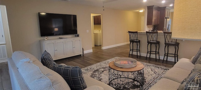 living room featuring dark wood-style flooring, washing machine and dryer, and baseboards