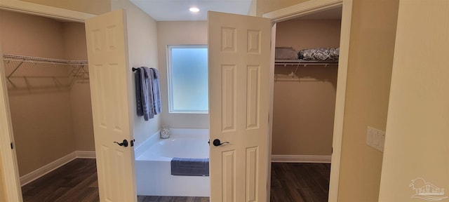 full bath with wood finished floors, a walk in closet, a bath, and baseboards