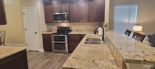 kitchen featuring light stone counters, a breakfast bar area, stainless steel appliances, dark wood-type flooring, and a sink