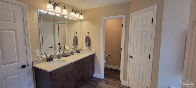 bathroom featuring toilet, wood finished floors, a sink, baseboards, and double vanity