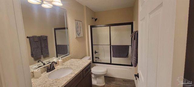 full bath with a textured wall, vanity, toilet, and bath / shower combo with glass door