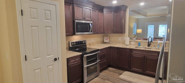 kitchen featuring light stone countertops, light wood-style floors, stainless steel appliances, and a sink