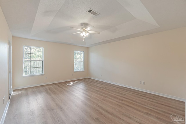 empty room featuring ceiling fan, a textured ceiling, a tray ceiling, and light hardwood / wood-style floors