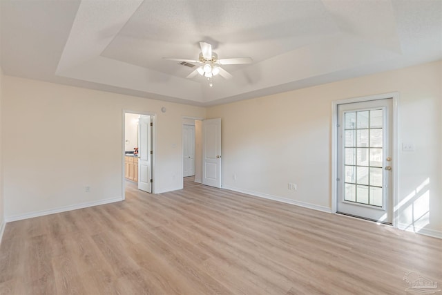 unfurnished room with ceiling fan, a textured ceiling, a tray ceiling, and light hardwood / wood-style floors