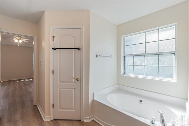 bathroom with ceiling fan, a bathing tub, and hardwood / wood-style floors