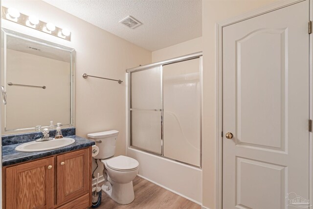 full bathroom with vanity, a textured ceiling, wood-type flooring, combined bath / shower with glass door, and toilet