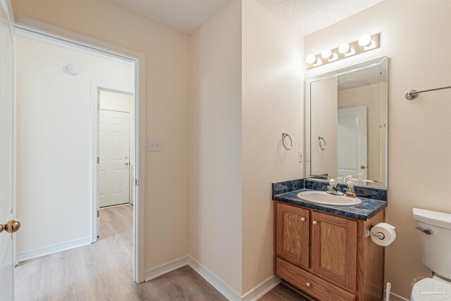 bathroom with wood-type flooring, a textured ceiling, vanity, and toilet