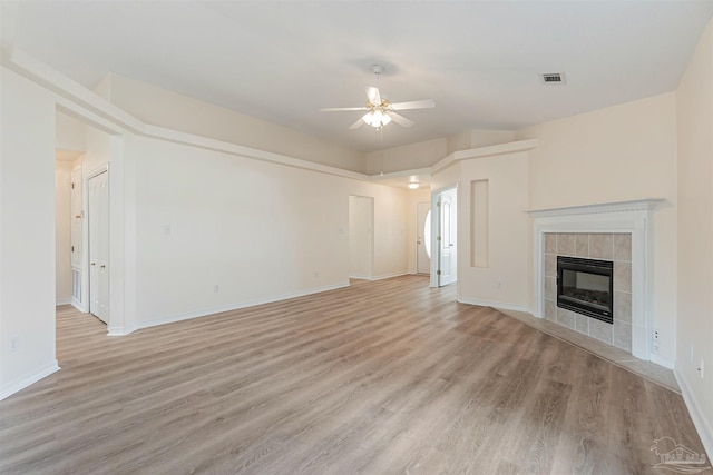 unfurnished living room with visible vents, light wood-style floors, a tiled fireplace, and a ceiling fan