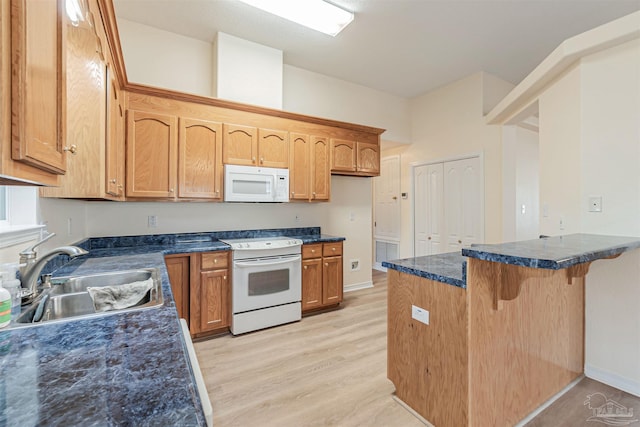 kitchen featuring white appliances, a peninsula, a sink, light wood-style floors, and a kitchen bar