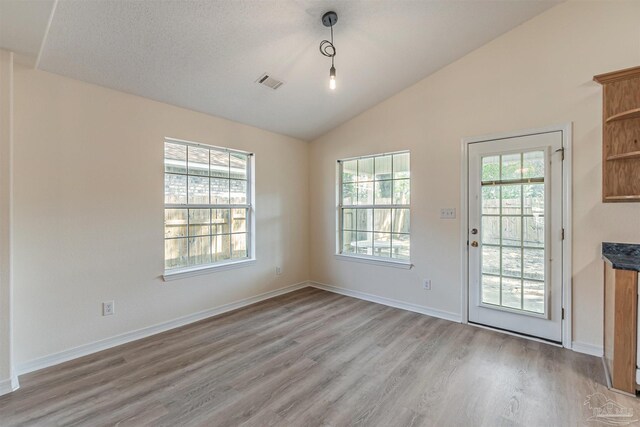 unfurnished dining area featuring lofted ceiling, light hardwood / wood-style floors, and a textured ceiling