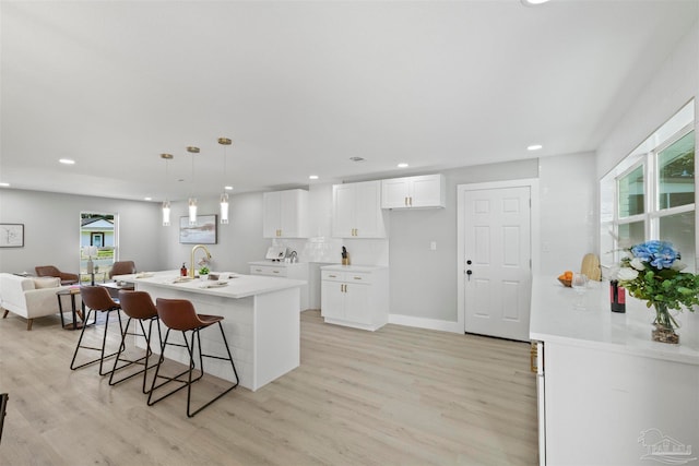 kitchen featuring white cabinetry, a healthy amount of sunlight, a center island with sink, and pendant lighting