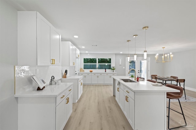 kitchen featuring an island with sink, hanging light fixtures, sink, light wood-type flooring, and white cabinetry