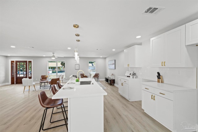 kitchen featuring decorative backsplash, an island with sink, decorative light fixtures, light wood-type flooring, and ceiling fan