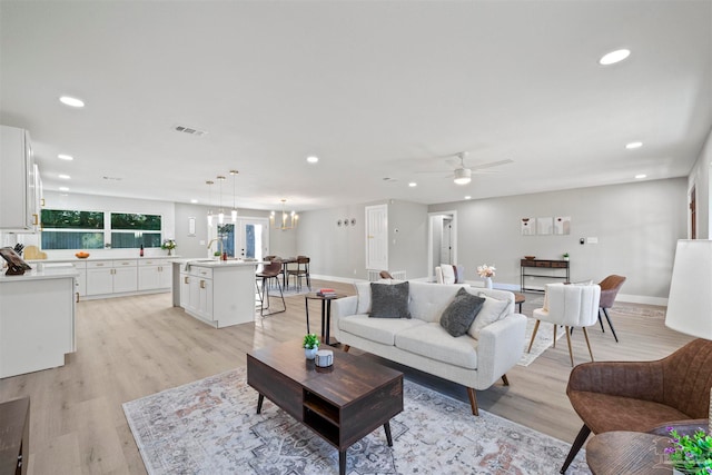 living room with light wood-type flooring and ceiling fan with notable chandelier