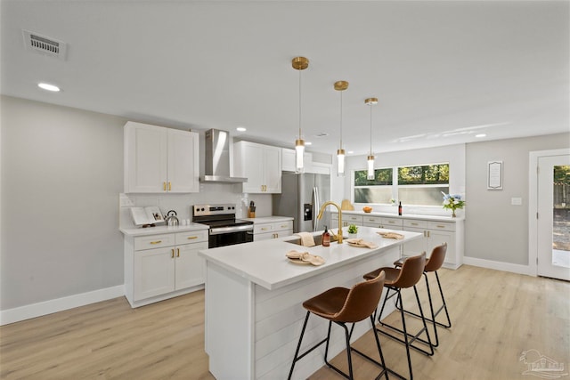 kitchen featuring stainless steel appliances, wall chimney exhaust hood, a breakfast bar, and white cabinets