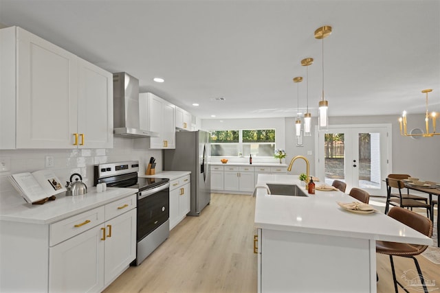 kitchen with appliances with stainless steel finishes, sink, hanging light fixtures, wall chimney exhaust hood, and a center island with sink