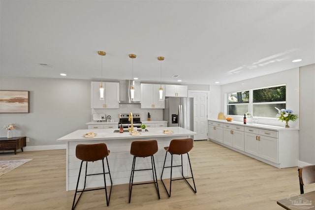 kitchen featuring white cabinets, wall chimney range hood, stainless steel appliances, and light hardwood / wood-style floors