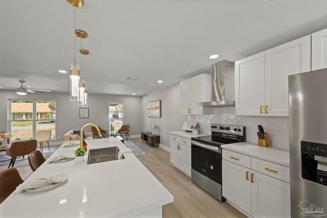 kitchen featuring appliances with stainless steel finishes, wall chimney exhaust hood, pendant lighting, light hardwood / wood-style flooring, and a kitchen island with sink