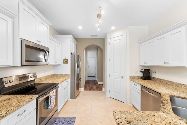 kitchen with light wood-type flooring, light stone counters, stainless steel appliances, and white cabinetry