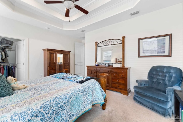 bedroom with a spacious closet, a closet, a tray ceiling, crown molding, and ceiling fan