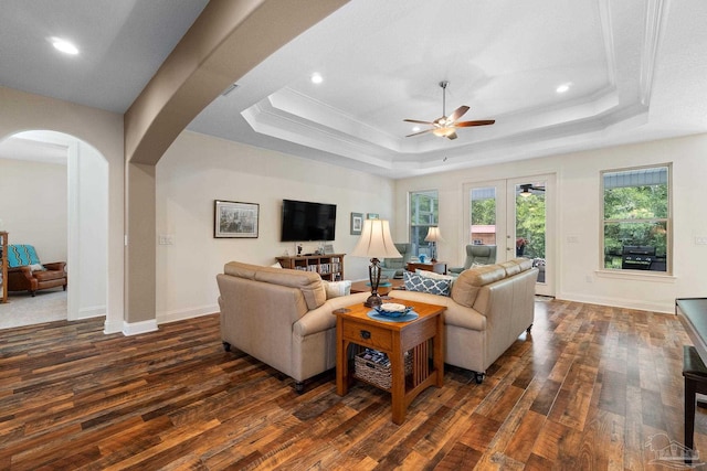 living room featuring dark wood-type flooring, a tray ceiling, ceiling fan, and crown molding