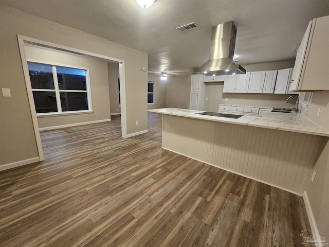 kitchen with dark hardwood / wood-style floors, white cabinetry, island exhaust hood, kitchen peninsula, and black electric cooktop