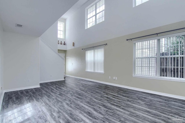 unfurnished living room featuring a towering ceiling and dark wood-type flooring