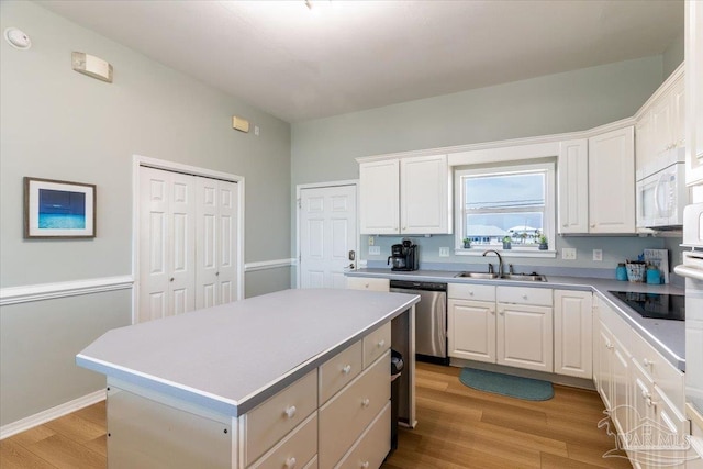 kitchen with a sink, stainless steel dishwasher, white cabinets, light wood finished floors, and black electric stovetop