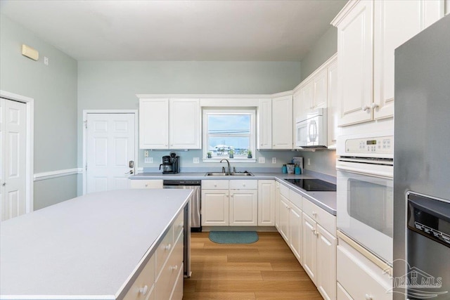 kitchen with light countertops, light wood-style flooring, white cabinets, white appliances, and a sink