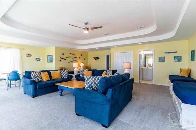 living area featuring a raised ceiling, carpet flooring, a ceiling fan, and baseboards