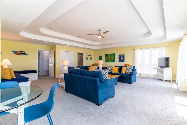 living room with visible vents, a raised ceiling, a ceiling fan, and carpet flooring