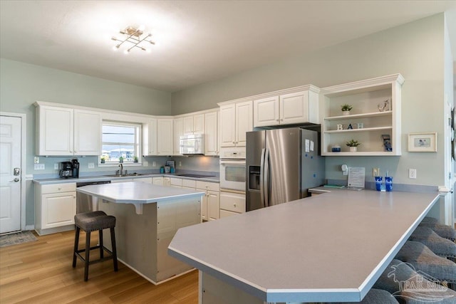 kitchen with a breakfast bar area, light wood finished floors, open shelves, stainless steel appliances, and white cabinets