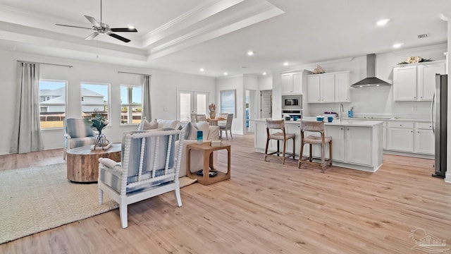 living room with crown molding, light wood-type flooring, visible vents, a raised ceiling, and recessed lighting