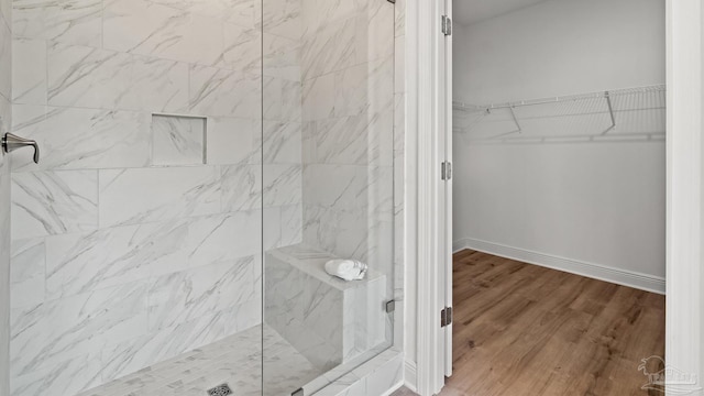 bathroom with a walk in closet, baseboards, wood finished floors, and a shower stall