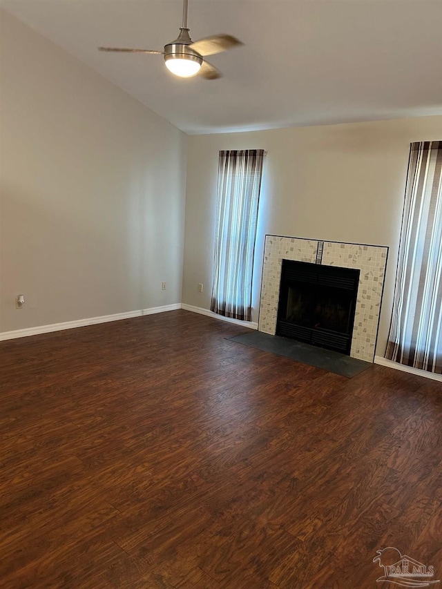 unfurnished living room with ceiling fan, baseboards, a tile fireplace, and dark wood-style floors