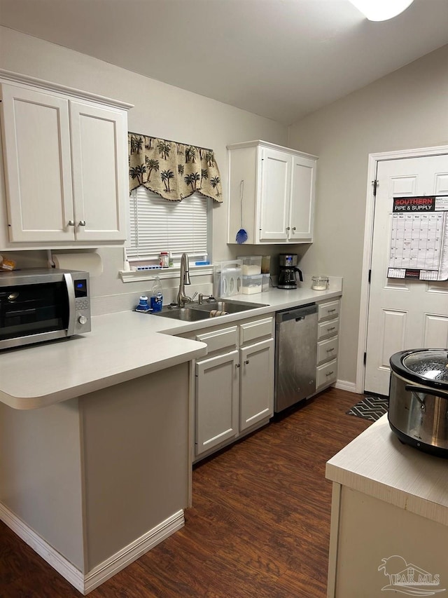 kitchen with white cabinets, appliances with stainless steel finishes, light countertops, a sink, and dark wood-style floors